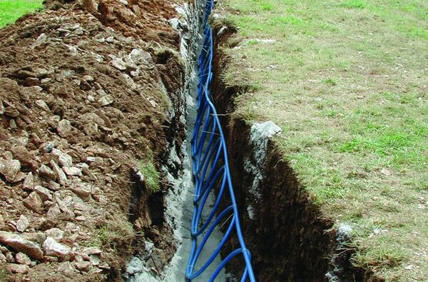 A blue slinky-coil ground loop pipe laid in a dug trench in a grassy garden for a ground source heat pump