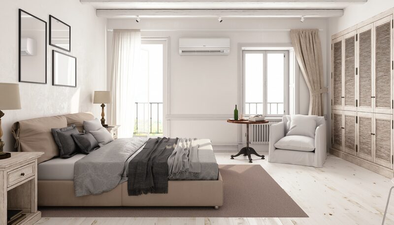 A wall-mounted split air conditioning unit installed high on the wall of a bright, neutrally decorated bedroom