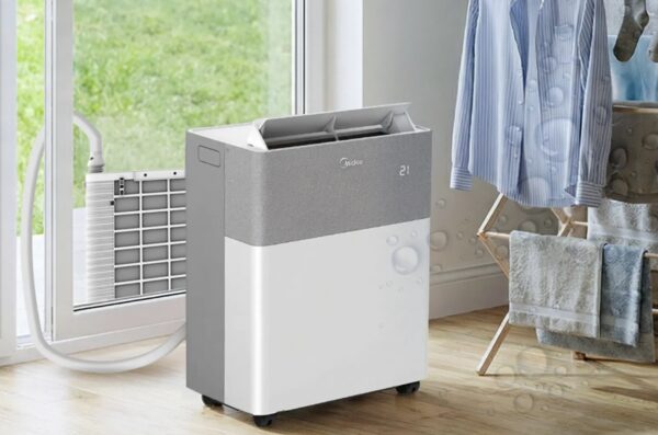 A Midea portable split air conditioner standing in a room next to a window with the outdoor unit visible outside