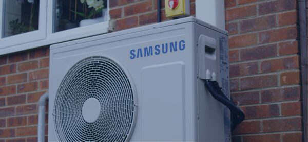 A Samsung air source heat pump unit installed on the outside brick wall of a house