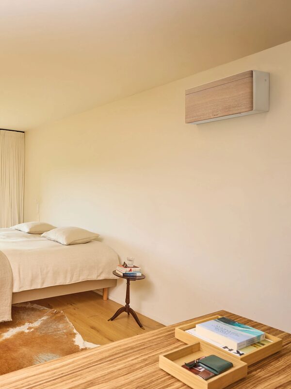 A wall-mounted Daikin air conditioning unit with a wood-effect panel installed high on the wall of a bright bedroom