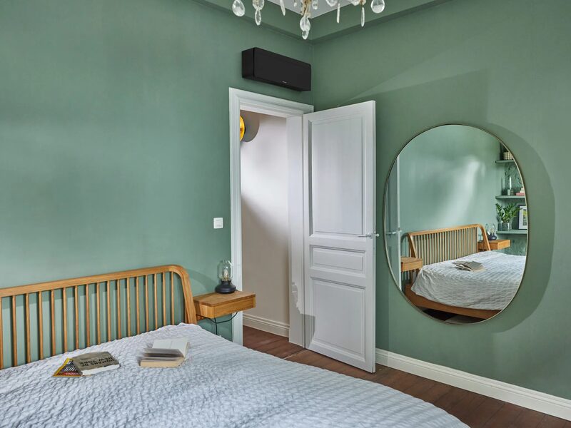 A wall-mounted air conditioning unit installed high on the wall of a green-painted bedroom