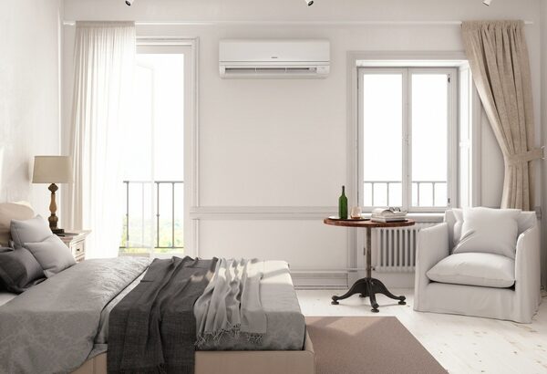 A wall-mounted air conditioning unit installed above a radiator in a bright white bedroom
