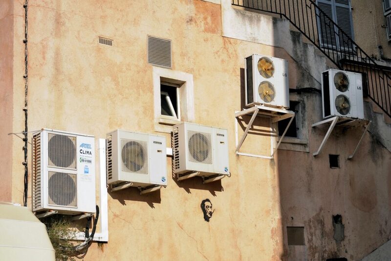 Several air conditioning condenser units mounted on the weathered exterior wall of a building