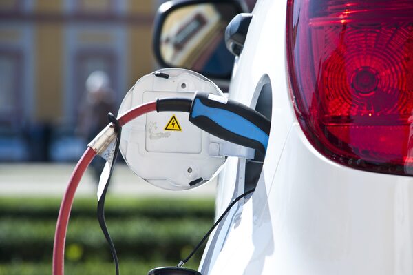 A charging cable plugged into the charging port of a white electric car
