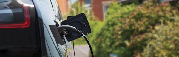 A black electric car plugged in with a charging cable in a residential driveway