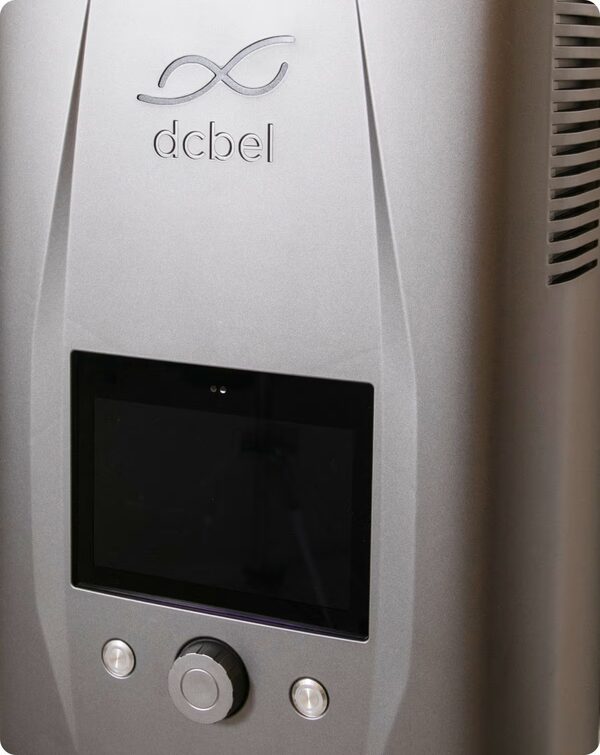 A close-up of the dcbel Ara bidirectional EV charger, a silver wall-mounted unit with a screen, dial and buttons