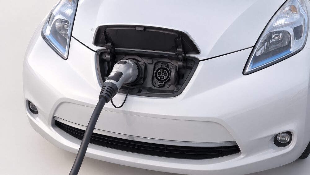 A close-up of the front of a Nissan Leaf with the small flap in the centre of the grille area open, revealing the CHAdeMO and Type 1 charging inlets side by side, with a tethered CHAdeMO charging cable plugged in.