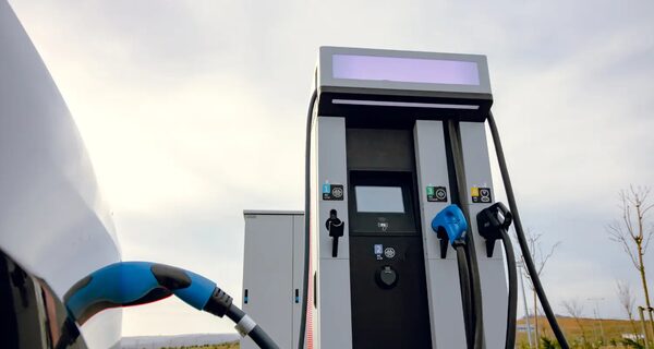 A public DC fast-charging station with two connector cables plugged into a white electric car