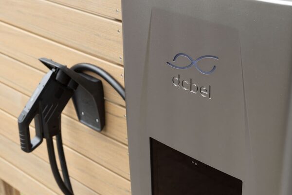 A grey dcbel Ara bidirectional EV charger mounted on a wooden-clad wall with its charging cable and holster