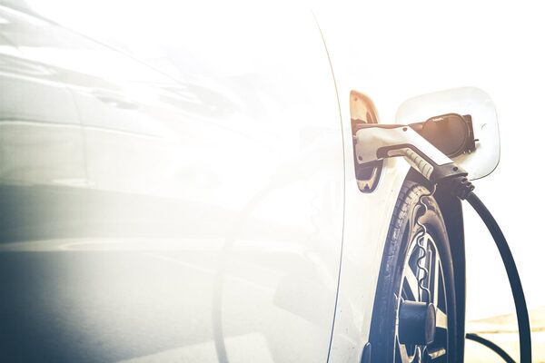 A charging cable plugged into the charging port of a white electric car