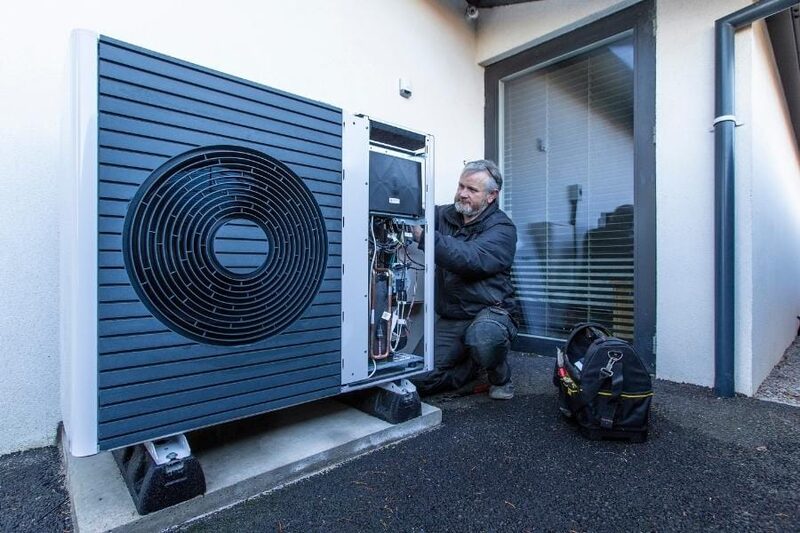 An engineer installing an air source heat pump outside a house