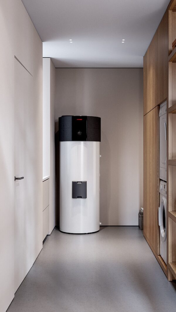 A white hot water cylinder with a black air-source heat pump unit on top, installed in a utility room next to a washing machine