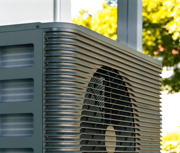 A close-up of an outdoor air source heat pump unit with a fan grille and louvred casing outside a house