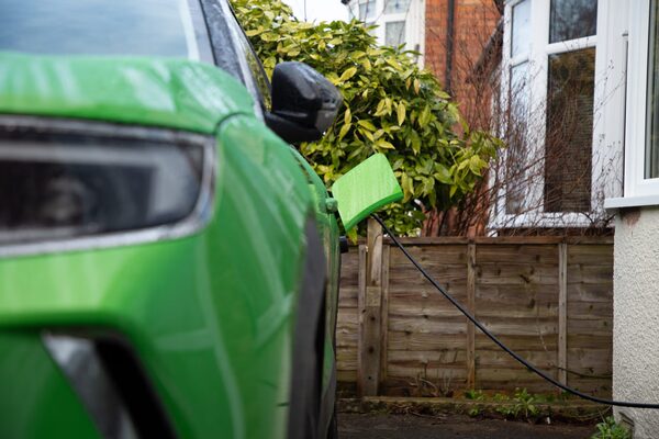 A green electric car charging on a UK driveway with a cable plugged into its charging port