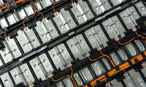A close-up of an electric car battery pack showing rows of lithium-ion cells connected by orange high-voltage cabling