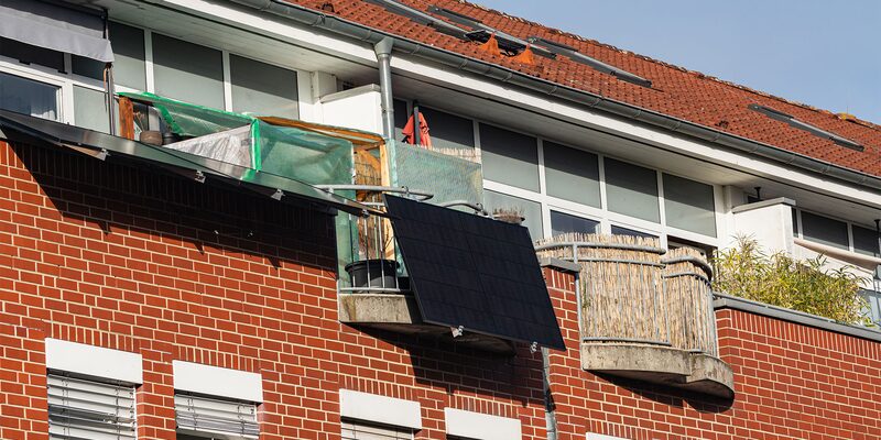 A plug-in solar panel mounted on the balcony of a brick apartment building