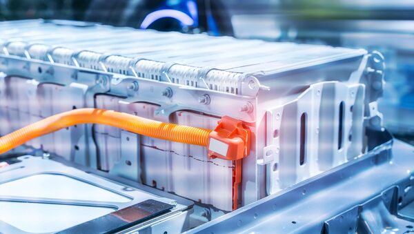 A close-up of an electric vehicle battery pack module with an orange high-voltage cable connector