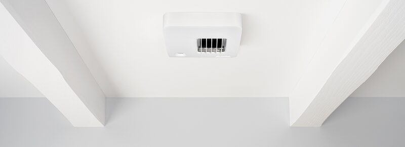 A white ceiling-mounted ventilation unit installed between beams on a white ceiling