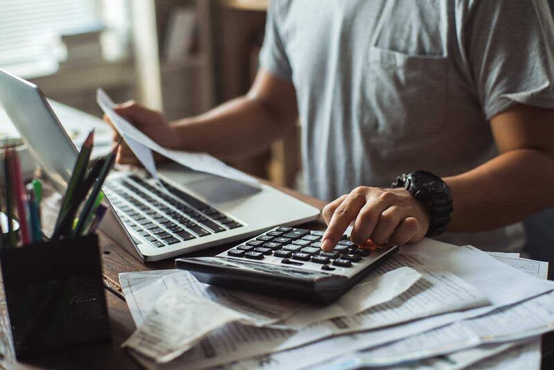 A person at a desk using a calculator and laptop while reviewing paper bills and receipts