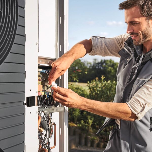 A technician servicing the internal wiring of an outdoor air source heat pump unit