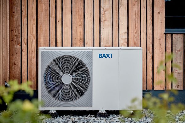 A white Baxi air source heat pump unit installed outside a house against a timber-clad wall