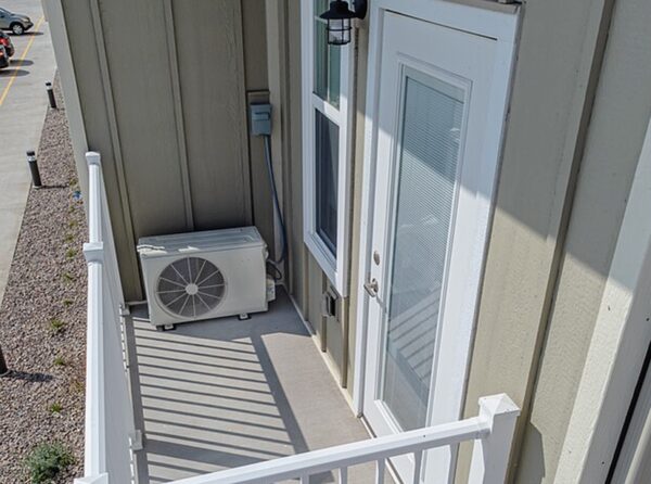 A white air source heat pump outdoor unit installed on a small concrete porch beside a house door