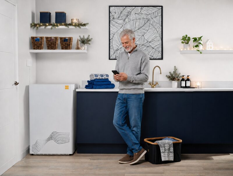A man using his phone in a utility room next to a white tepeo ZEB battery-style heater unit
