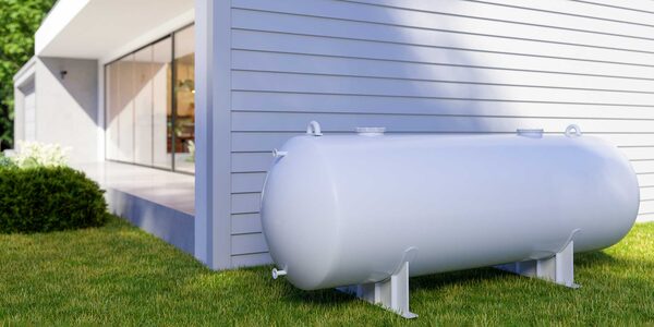 A white cylindrical heating oil tank on legs on a lawn beside a modern white house