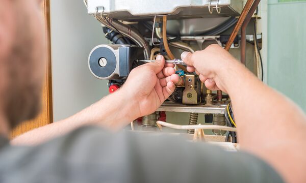 A heating engineer repairing the internal components of a wall-mounted gas boiler with a screwdriver