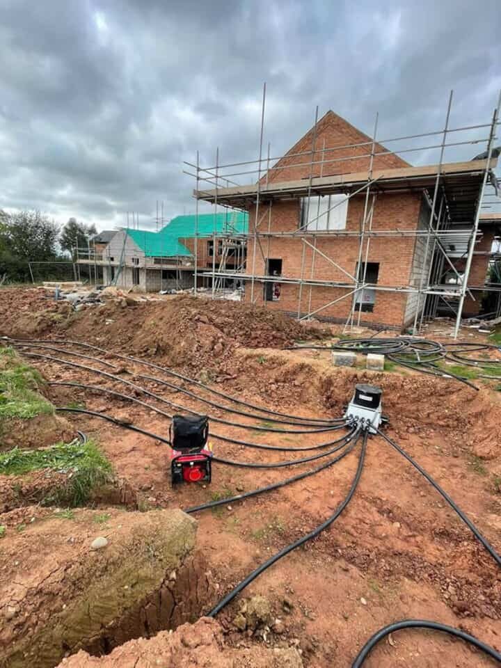 Ground source heat pump ground loop pipes being laid in a trench at a brick house under construction with scaffolding