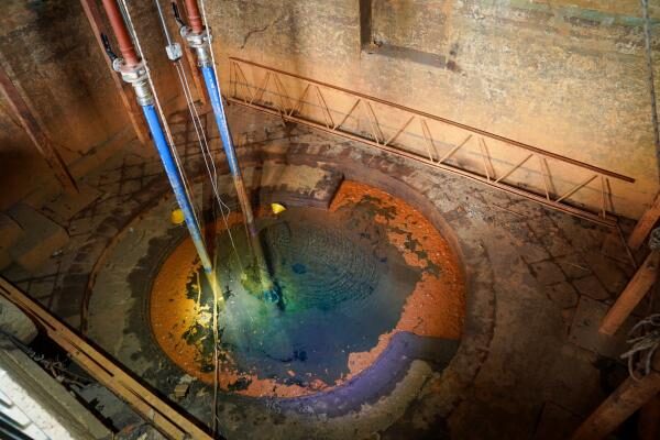 Pipes descending into a flooded mine shaft with rust-coloured water, part of a mine water heating scheme