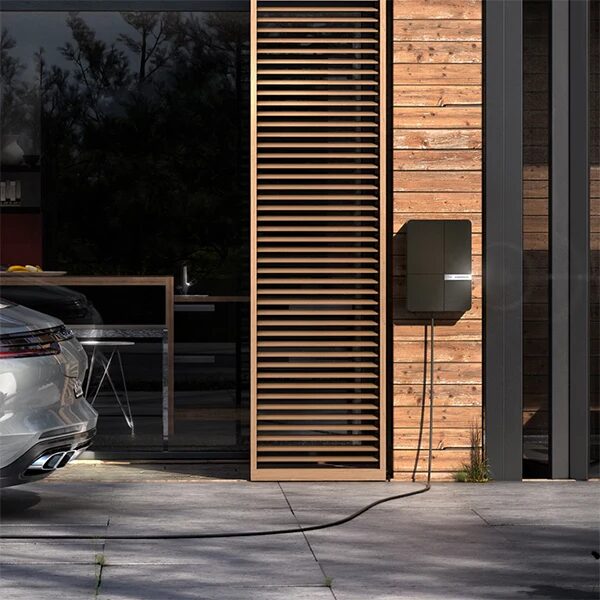 An Andersen A2 wall-mounted home EV charger on a timber-clad house wall with a cable running to a parked car