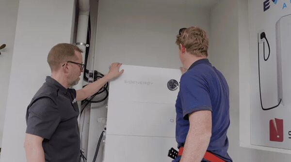 Two installers fitting a white Sigenergy home battery unit on an indoor wall