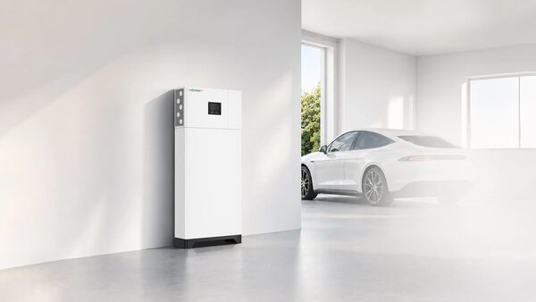 A tall white LuxpowerTek all-in-one home battery storage unit standing in a bright garage with a white electric car parked behind it