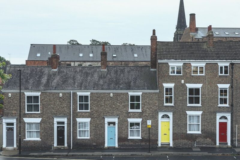 A row of traditional brick terraced houses with colourful front doors on a UK street