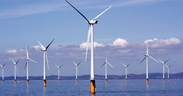 An offshore wind farm with many white wind turbines standing in the sea under a partly cloudy sky