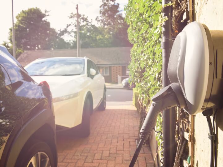 A wall-mounted electric car chargepoint with cable on a driveway beside parked cars