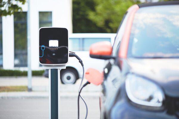 An electric car charging point on a post with a cable plugged into a parked car