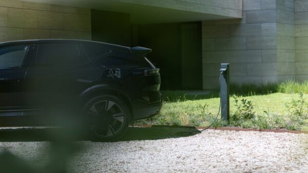 A dark electric car charging from a home EV charge point outside a modern house