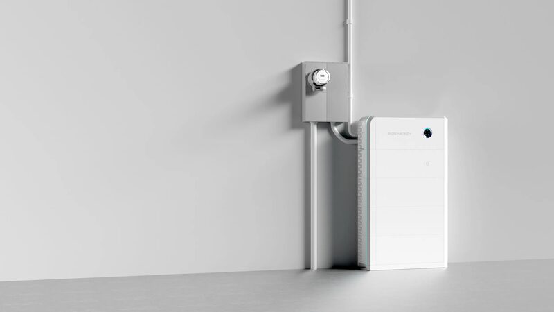 A white wall-mounted home battery unit installed next to an electrical meter box on a plain grey wall