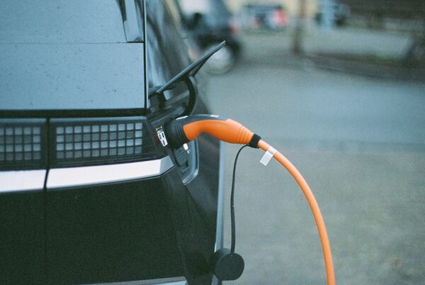 An electric car being charged with an orange cable plugged into its rear charging port outdoors
