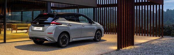 A grey Nissan Leaf electric car parked outside a modern house at dusk
