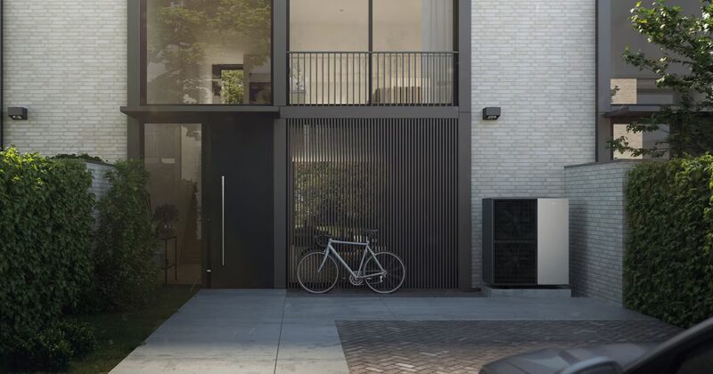 A Viessmann Vitocal 150-A air source heat pump unit installed outside a modern brick townhouse beside a slatted garage door with a bicycle parked in front