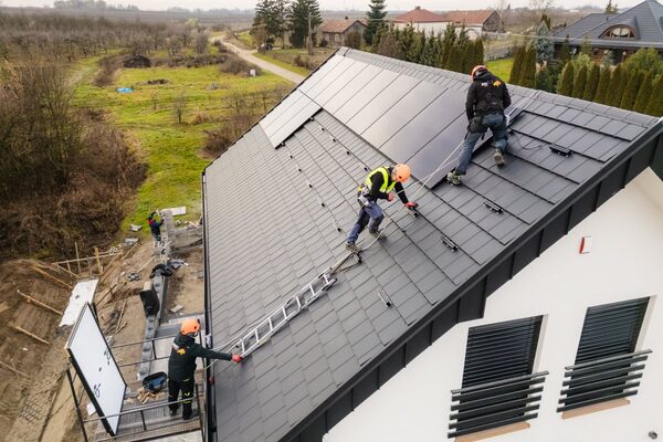 Installers fitting solar panels on the tiled roof of a new house