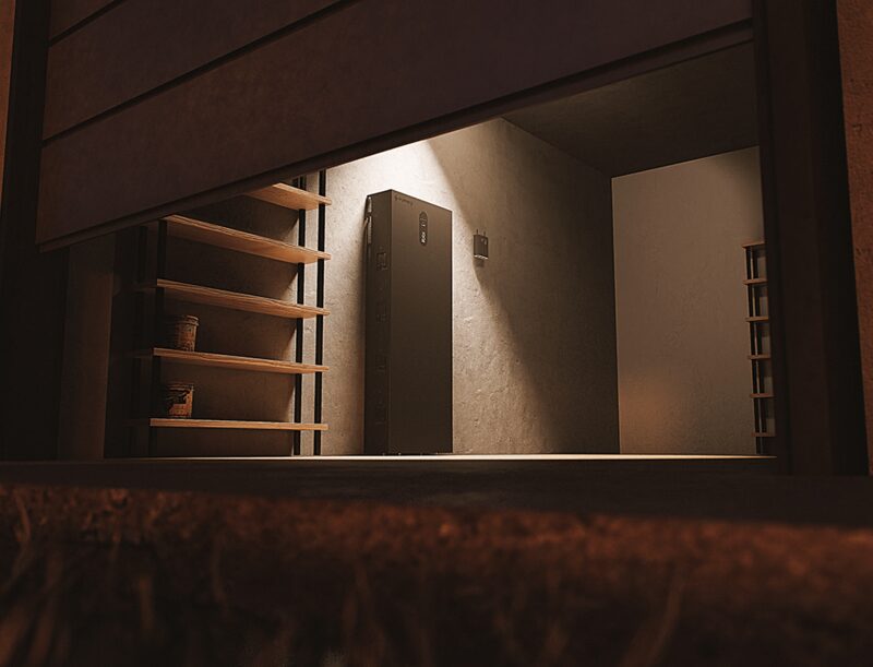 A tall black home battery unit mounted on the wall of a dimly lit garage