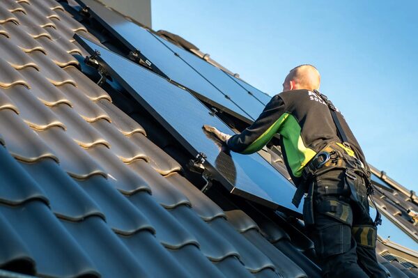 A solar installer fitting a solar panel onto a tiled roof