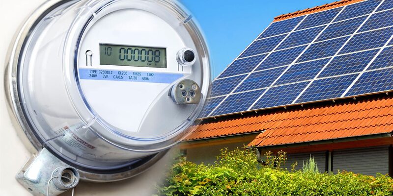 A close-up of an electricity meter beside a house roof covered with solar panels
