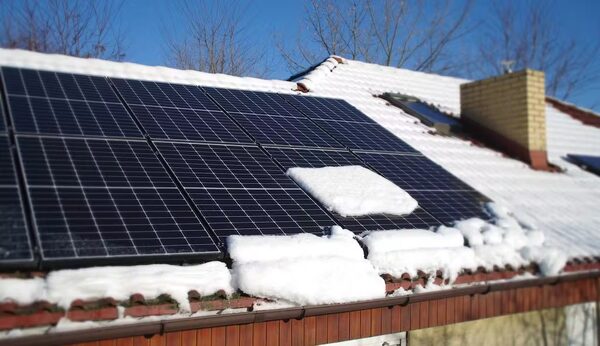 Snow-covered rooftop solar panels on a tiled house roof in winter