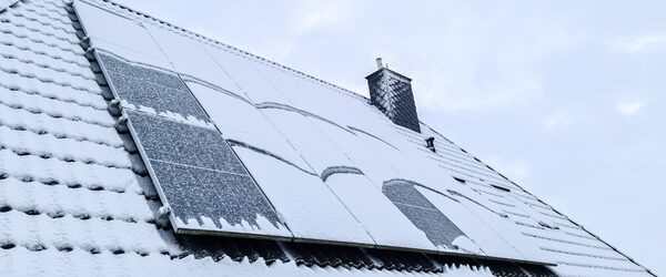 Snow-covered solar panels on a tiled roof next to a chimney in winter